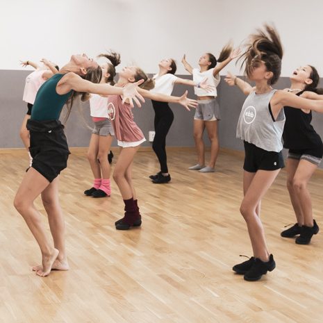 Profesora de baile de Barcelona vestida de negro realizando la clase de baile moderno con chicas adolescentes en el aula de la escuela de baile