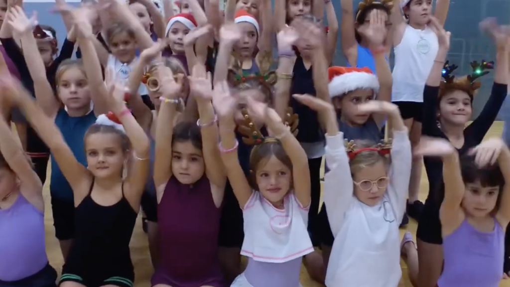 Grupo de niñas bailando durante el cursillo de Navidad en la Escuela Esther Bosch, con gorros y complementos navideños